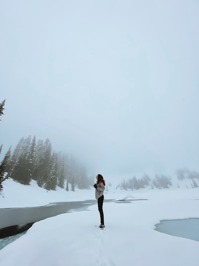 白天，穿着白色夹克和黑色裤子的女人站在白雪覆盖的地面上